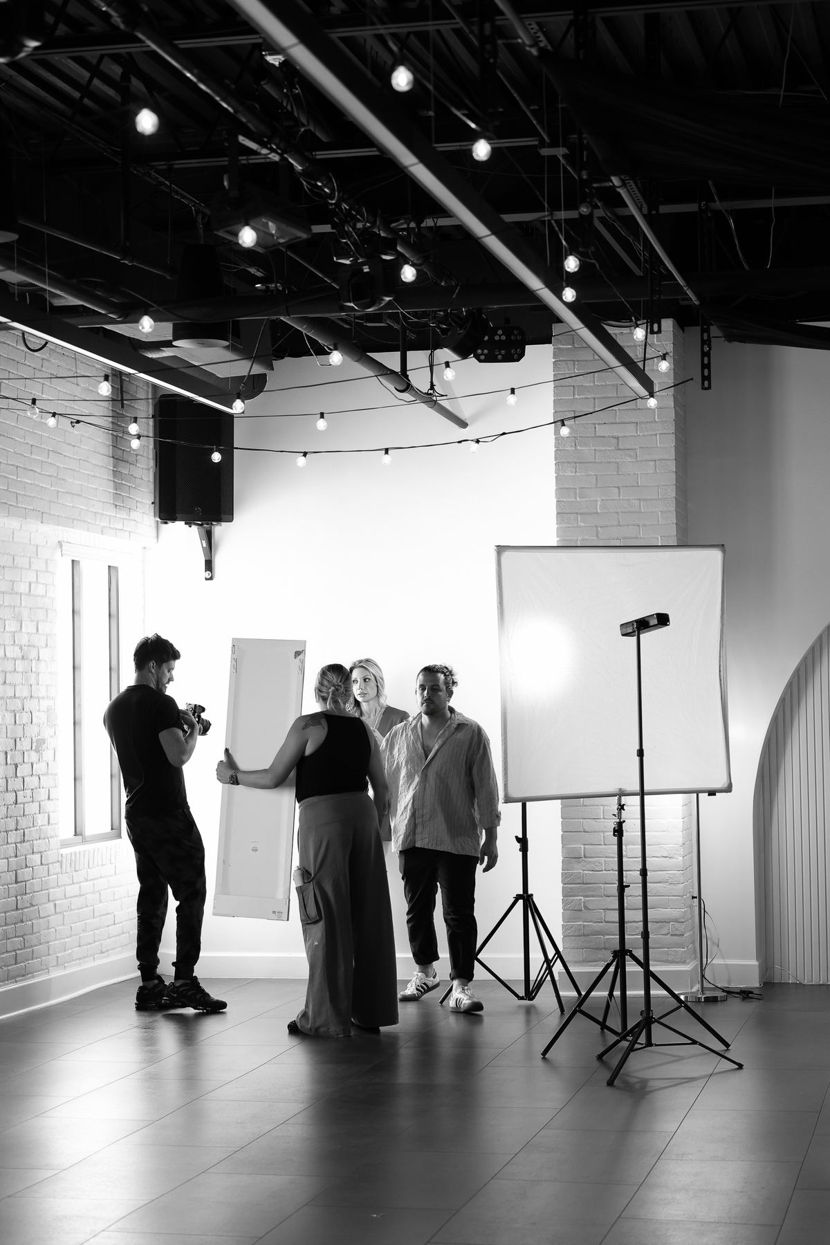 A photographer, model and crew working with studio lights in the open hall at Trellis 925, in black and white