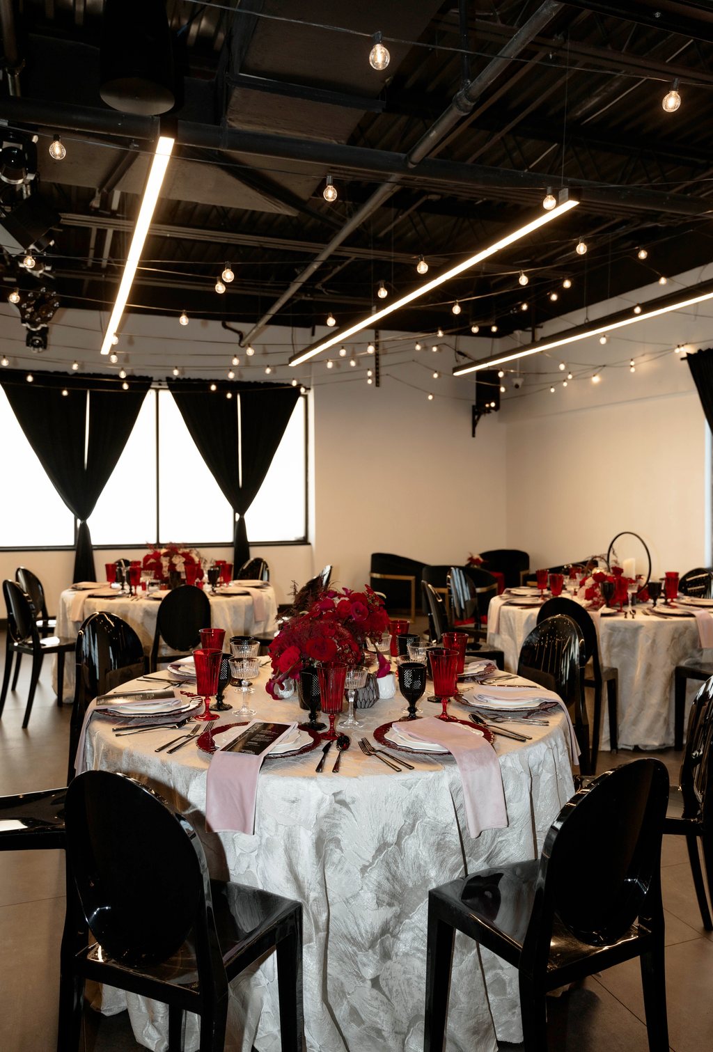 Round tables set in red and white beneath string lights at Trellis 925